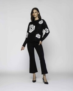 Vista completa de sweater negro con rosas blancas tejidas en frente y mangas, combinado con pantalón acampanado y tacones