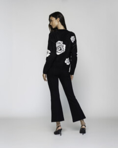 Vista posterior del sweater negro con rosas blancas tejidas visibles en espalda y mangas, modelo Formentera