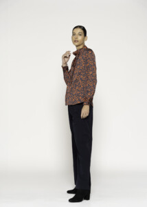 Vista lateral de modelo con camisa estampada en naranjas y negros sobre pantalón negro, fondo blanco