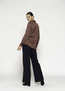Vista lateral de tres cuartos de blusa con estampado floral en tonos caramelo y negro, pantalón palazzo negro de tiro alto y corte amplio