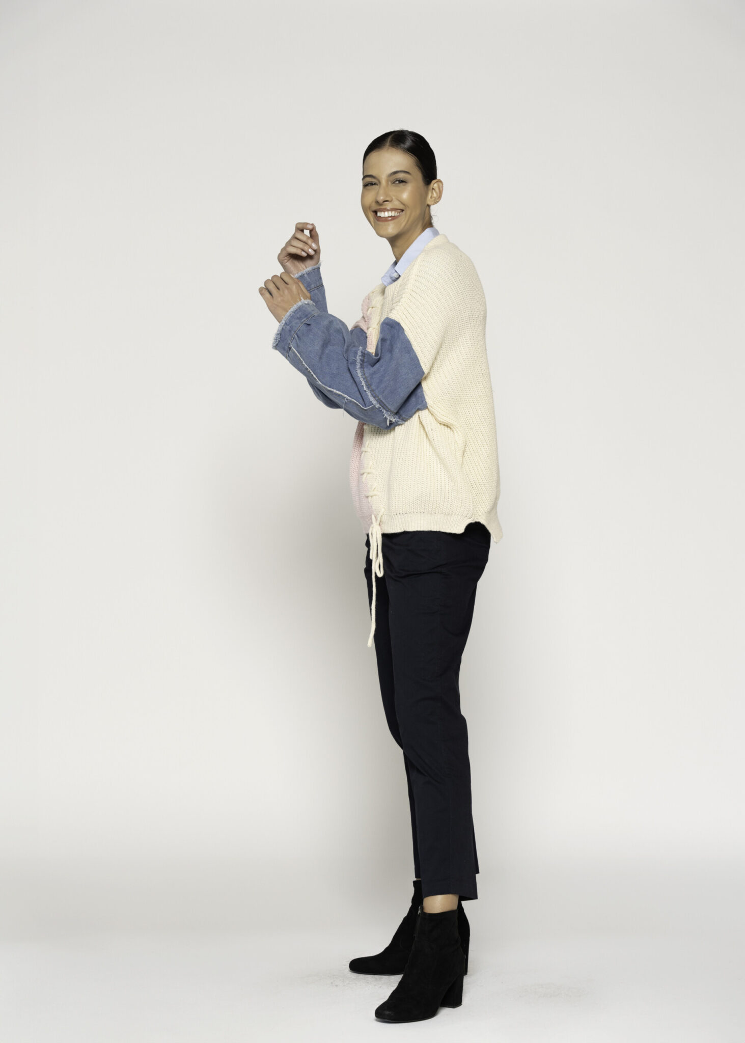 Vista lateral de sweater tejido con bloques crema y rosa, mangas desmontables de mezclilla azul y cordón de ajuste visible