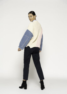 Vista de espaldas del sweater tricolor con bloques en tejido crema y rosa, mangas de mezclilla azul desmontables visibles, combinado con pantalón negro y botines.