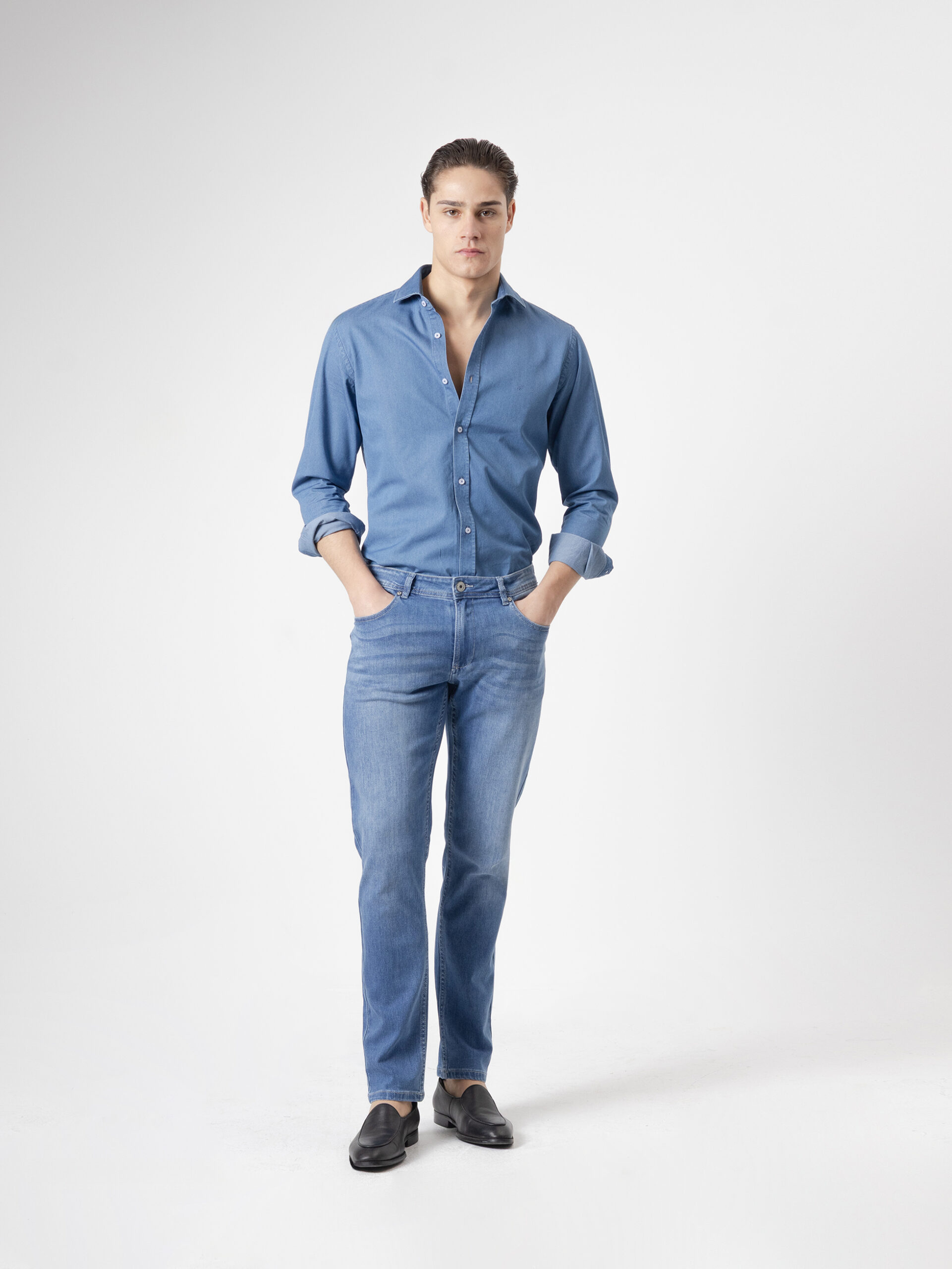 Jeans slim fit azul medio de PuroEgo en denim, de cuerpo entero y de frente, con camisa de mezclilla y mocasines negros.