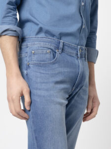 Detalle del jeans slim fit azul medio de PuroEgo: bolsillo relojero con remaches, pespunte tostado y botón de metal en la pretina.
