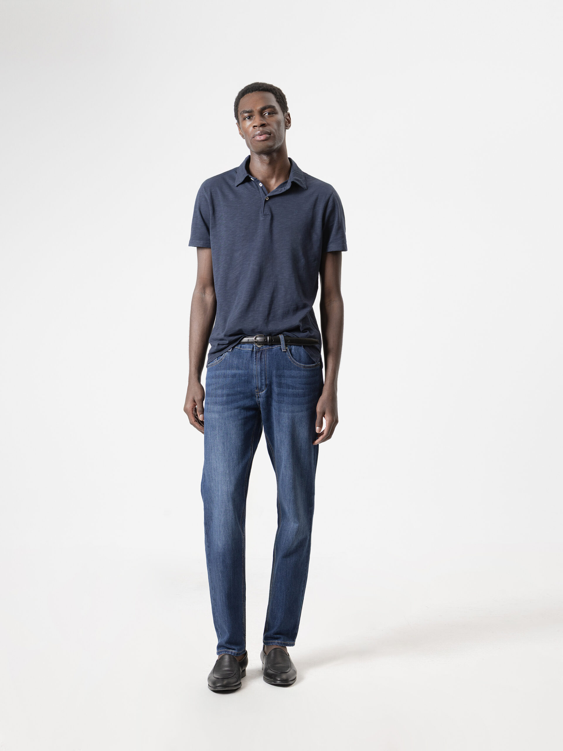 Jeans slim fit azul oscuro de PuroEgo con efecto desgastado, de cuerpo entero y de frente, con polo azul y cinturón negro.