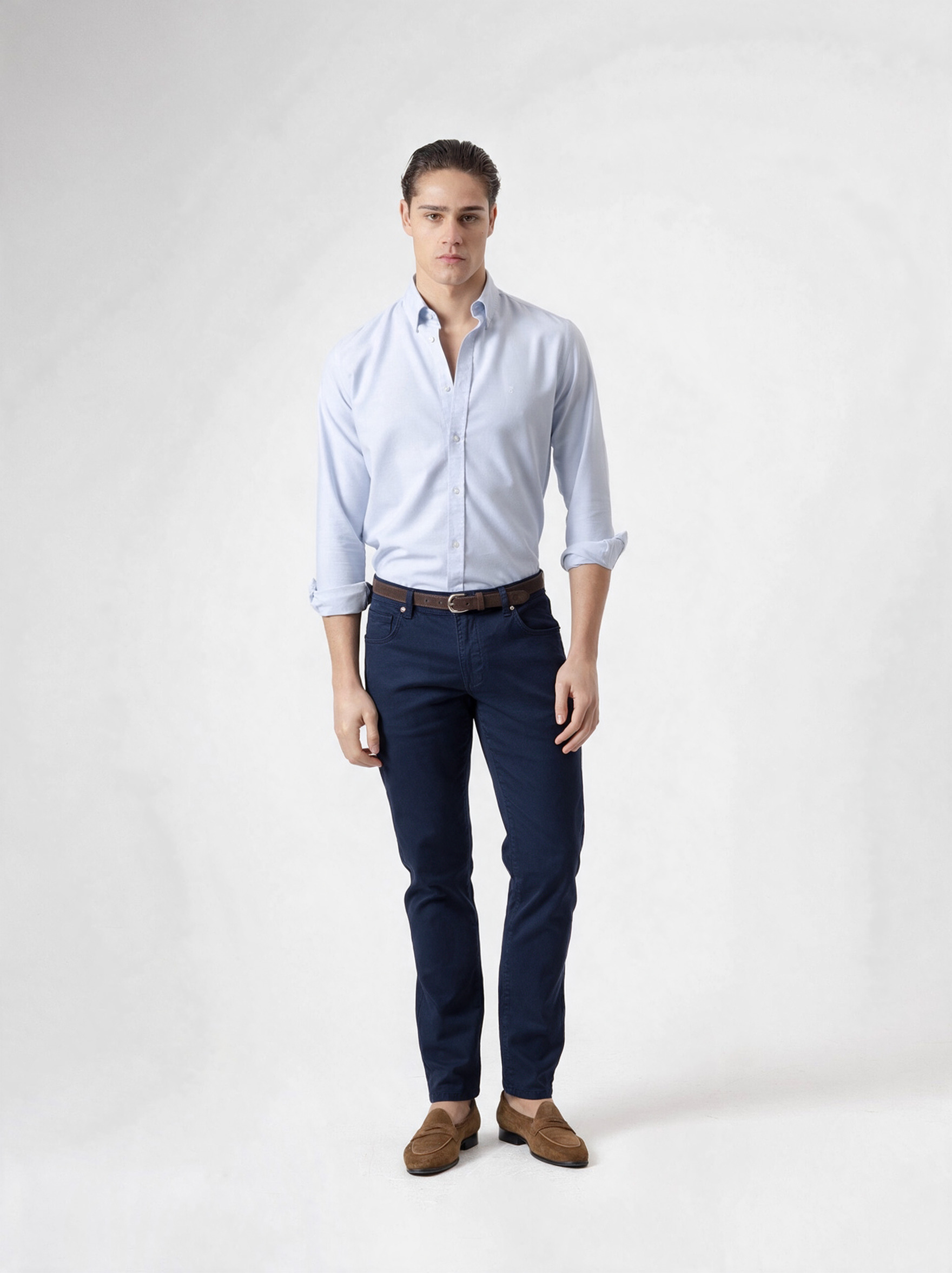 Pantalón cinco bolsillos azul marino de PuroEgo, de cuerpo entero y de frente, con camisa celeste, cinturón café y mocasines de gamuza.