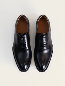 El par de zapatos oxford negros de PuroEgo visto desde arriba, con la puntera con costura, el cordonaje y la plantilla de piel