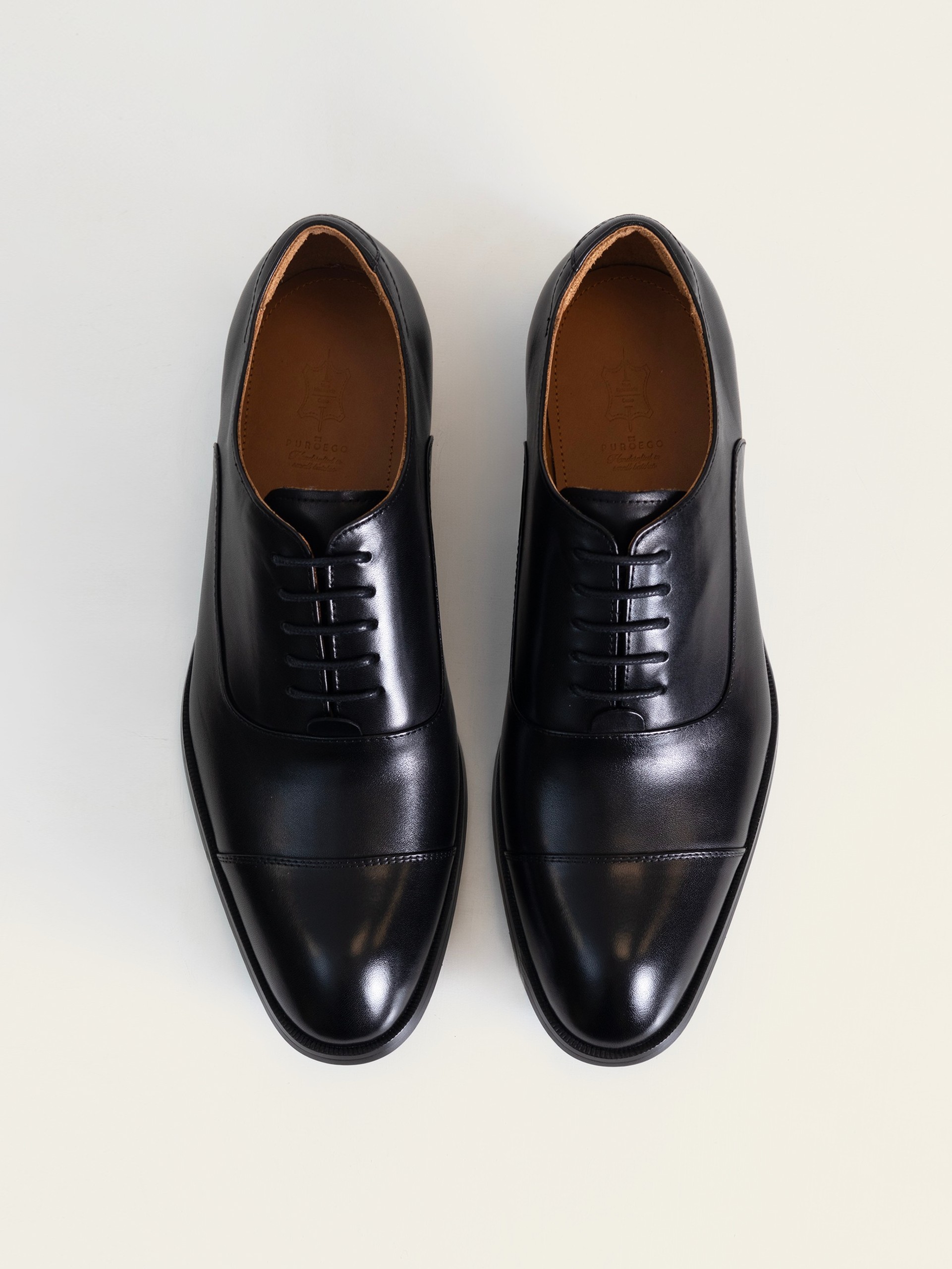 El par de zapatos oxford negros de PuroEgo visto desde arriba, con la puntera con costura, el cordonaje y la plantilla de piel