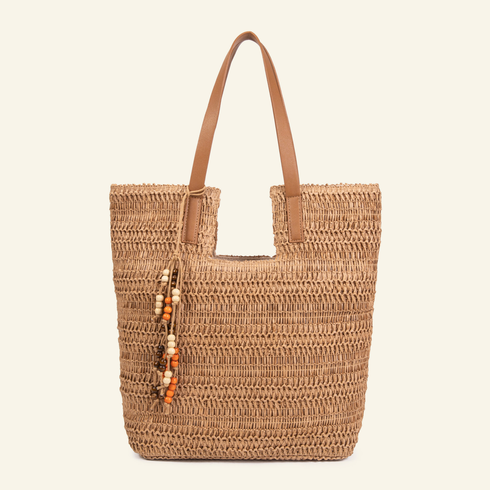 Bolso de rafia beige de Formentera visto de frente sobre fondo blanco, con asas de cuero café y colgante de mostacillas de madera crema, naranja y café.