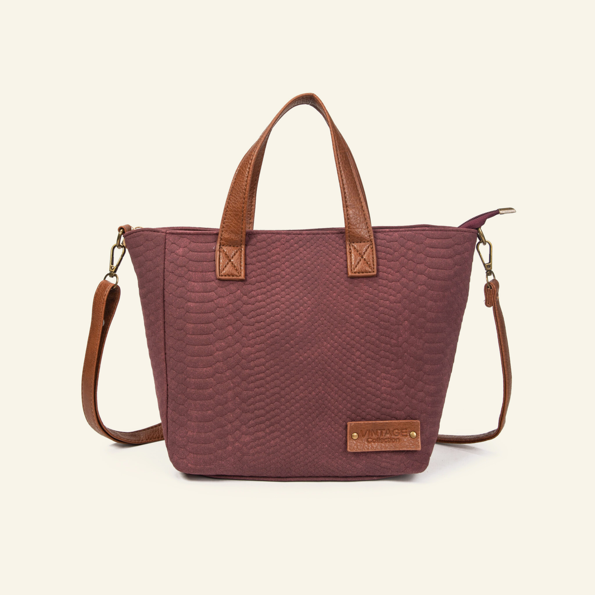 Bolso Formentera color vino con textura de reptil, de frente: asas y correa larga de cuero café y placa metálica.